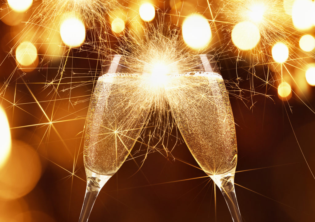 Glasses of champagne and sparklers on bright background with bokeh effect